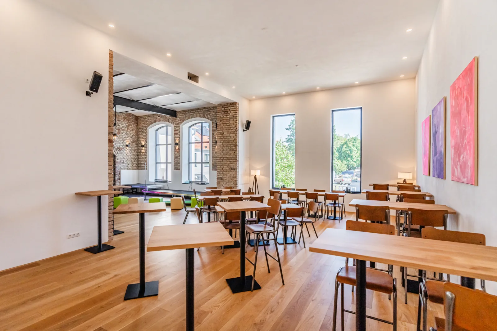 Der Saal der Brennerei Pentenried mit Stehtischen, Holzboden und hohen Fenstern